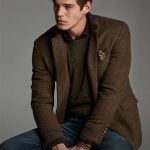 Man layers brown herringbone blazer over green cable-knit sweater .